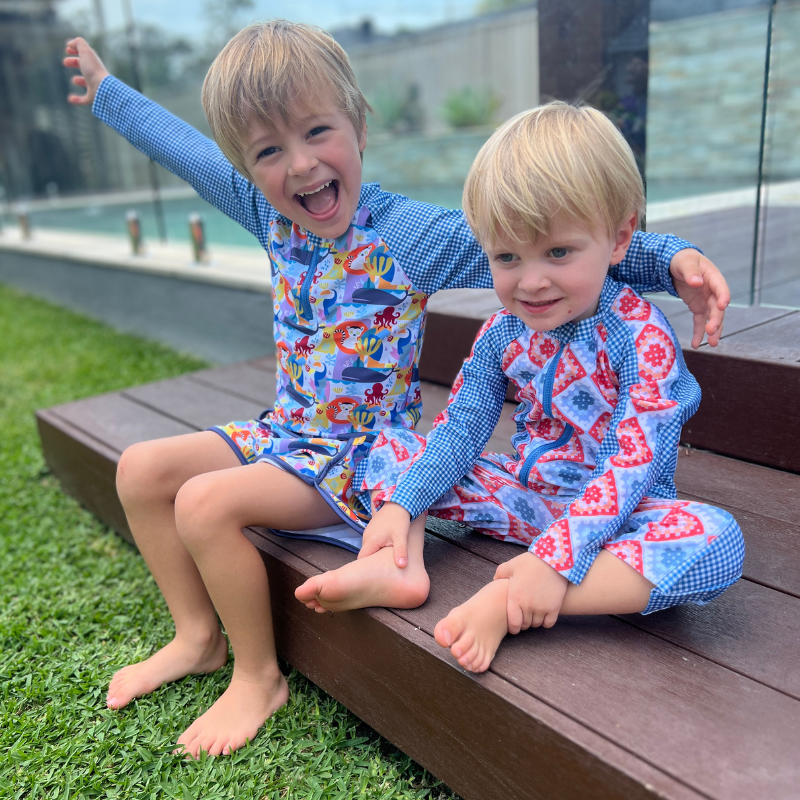 Two children in tyoub swim suits sitting on a wooden step outdoors.