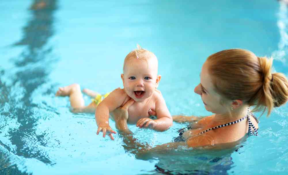 Young baby learning to swim in pool with women