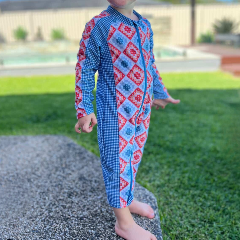 Child wearing a colorful patterned onesie standing on a gravel path with grass in the background.