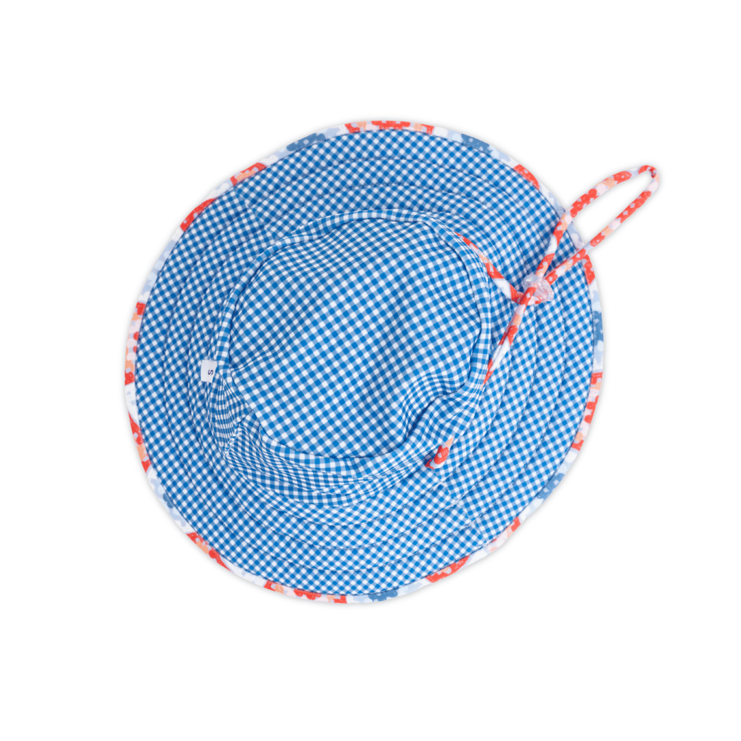 Inside view of Tyoub kids’ wide brim bucket hat, lined with contrasting blue gingham checker print, showing neat stitching, chin strap snap closure, crafted from sustainable recycled polyester swim fabric. Clear plastic toggle clip, adjustable drawstring to keep hat on.